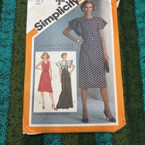 Pode incluir: Padrão de costura Simplicity vintage com um design de vestido de bolinhas. O pacote é laranja e branco, com ilustrações de três estilos de vestidos. O texto no pacote diz "Simplicity" e "Jonathan Hitchcock for Reuben Thomas."