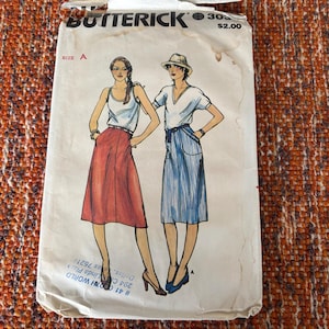 Può includere: Modello di cucito Butterick vintage con illustrazioni di due donne con gonne e top. Il modello è etichettato "30" e "TAGLIA A". Il prezzo è di $2,00. Il modello è su una superficie arancione e marrone strutturata.