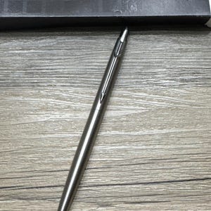 May include: A silver Parker mechanical pencil with a black arrowhead design on the top.