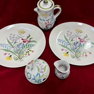 May include: A set of white ceramic dishes with a floral design in shades of pink, blue, green, and yellow. The set includes two large plates, a small creamer, and a sugar bowl with a lid.