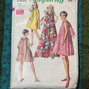 May include: Vintage Simplicity sewing pattern envelope featuring illustrations of dresses. The envelope is white with the text "7651 Simplicity" and "Miss Medium 12-14". The dresses are in yellow, floral, red plaid, and striped patterns.