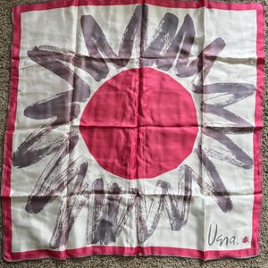 May include: Square silk scarf with a sunburst design. The scarf features a large pink circle in the center, surrounded by gray brushstroke-style rays on a white background. A pink border frames the design. The scarf has the word "Usna" in the corner.