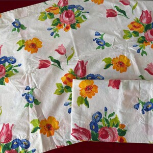 May include: Two white cotton pillowcases with a floral pattern featuring pink, yellow, blue, and green flowers. The pillowcases are made of a soft, comfortable fabric and are perfect for adding a touch of elegance to any bedroom.