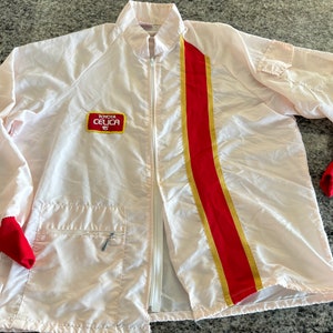 May include: White nylon jacket with a red and gold stripe down the right side. The jacket has a zipper closure and a pocket on the left side. The jacket has a red patch on the left chest that says "TOYOTA CELICA TS".