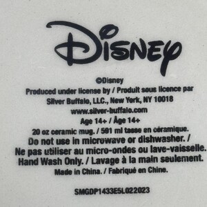 May include: A white ceramic mug base featuring black printed text that reads Disney, Produced under license by Silver Buffalo, LLC., New York, NY 10018, 20 oz ceramic mug, Do not use in microwave or dishwasher, Hand Wash Only, Made in China, SMGDP1433E5L022023.