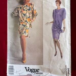 Könnte beinhalten: Vogue Patterns 2680 Schnittmuster für ein Kleid von Emanuel Ungaro. Das Schnittmuster enthält zwei Ansichten: ein Kleid mit Blumenmuster und langen Ärmeln und ein einfarbiges lila Kleid mit kurzen Ärmeln. Das Schnittmuster ist für die Größen 12, 14 und 16.