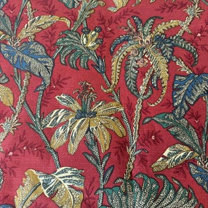 Könnte beinhalten: Nahaufnahme eines roten Stoffes mit einem botanischen Muster. Das Design zeigt große, stilisierte Blätter und Blüten in Grün-, Gold- und Blautönen. Die Ästhetik erinnert an Vintage-Textilien und tropische Themen.