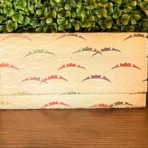 May include: A beige wallet with a repeating pattern of red, green, and purple waves. The wallet is closed and has a flap.