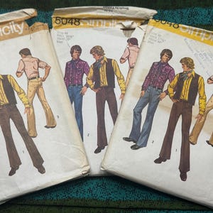 May include: Three vintage Simplicity sewing pattern envelopes. Each envelope features a retro illustration of a man in a patterned shirt, vest, and flared pants. The envelopes are cream-colored with yellow and black text.