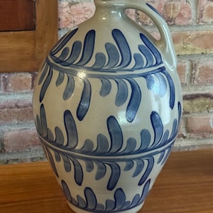 May include: A gray stoneware jug with a blue and white leaf design. The jug has a wide mouth and a handle.