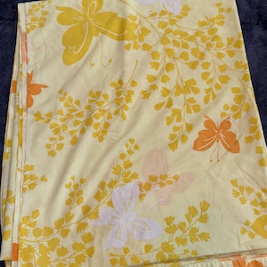May include: A folded, light yellow sheet with a repeating pattern of stylized butterflies and floral sprigs in shades of yellow, orange, and white. The sheet is made of a soft, possibly cotton, fabric.
