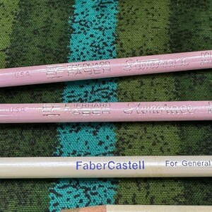 May include: Close-up of four pencils. Two are light pink with "Eberhard Faber" and "Stenotrace" printed on them. One is white with "Faber-Castell" printed on it. The last is white with "FABER ERASER STICK" printed on it.