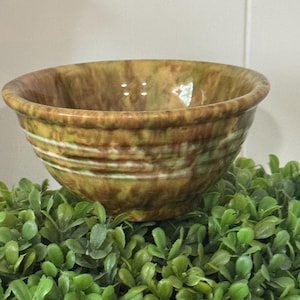 May include: A ceramic bowl featuring a mottled glaze in shades of brown, tan, and olive green. The exterior surface displays a series of horizontal ridges encircling the body, creating a textured appearance with a glossy finish throughout the piece.