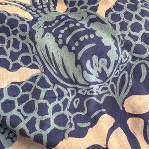 May include: Close-up of fabric with a repeating pattern of stylized pineapples in shades of navy blue and teal. The design is printed on a light beige background, creating a tropical and artistic aesthetic. The fabric appears to be soft and flowing.