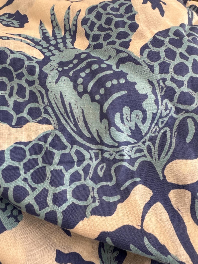 May include: Close-up of fabric with a repeating pattern of stylized pineapples in shades of navy blue and teal. The design is printed on a light beige background, creating a tropical and artistic aesthetic. The fabric appears to be soft and flowing.