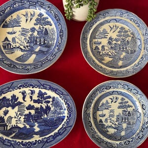 May include: Four blue and white willow pattern plates. Two are round and two are oval. The plates have a blue and white design with a willow tree, a pagoda, and a river.