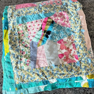 May include: A patchwork quilt with a variety of floral patterns in shades of pink, blue, and green. The quilt is made of different fabrics and textures, and the edges are finished with a turquoise border.