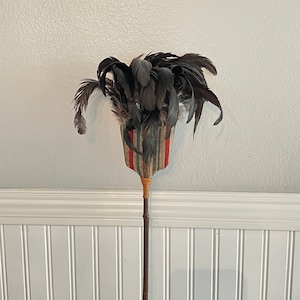May include: A vintage feather duster with a black and white striped fabric handle and a long wooden shaft.
