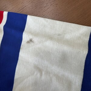 May include: A white, blue and red striped fabric with two small dark brown stains.