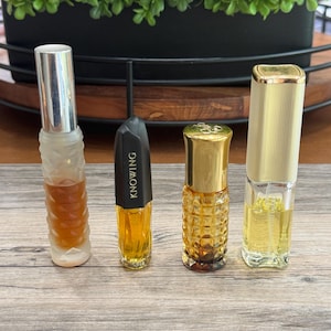 May include: Four vintage perfume bottles of varying shapes and sizes. The bottles are filled with amber and yellow liquids. One bottle has the word "KNOWING" printed on it. The bottles are arranged on a wooden surface.