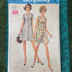 Könnte beinhalten: Ein Vintage-Schnittmusterumschlag von Simplicity 8218 mit Illustrationen von zwei Kleidern. Ein Kleid hat ein schwarz-weißes Karomuster, das andere einen bunten Blumendruck. Der Umschlag enthält Texte wie 8218, Simplicity und 75c.