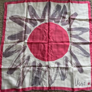 May include: A square silk scarf with a white background, featuring a large pink circle in the center and gray brushstroke-style designs radiating outward. The scarf has a pink border and the word "Vana" is printed in the bottom right corner.