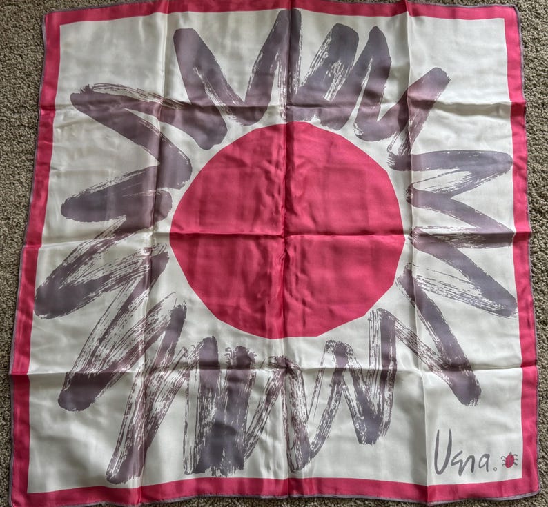 May include: A square silk scarf with a white background, featuring a large pink circle in the center and gray brushstroke-style designs radiating outward. The scarf has a pink border and the word "Vana" is printed in the bottom right corner.