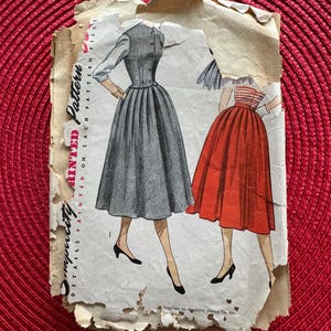 May include: Vintage Simplicity sewing pattern for a skirt with a gathered waist. The pattern is printed on a white paper with a red and white striped fabric design. The text on the pattern reads "Simplicity Printed Pattern", "Details Printed on Each Pattern Piece", and "Copyright by Simplicity Pattern Co. Inc."