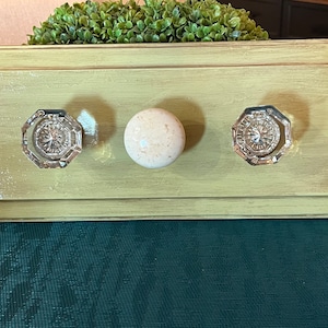 May include: A light green wooden frame with three knobs. Two of the knobs are clear glass with a silver finish and one is a white ceramic knob.