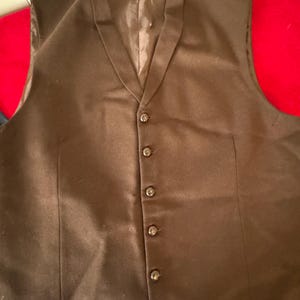 May include: A brown sleeveless vest with a V-neck and six buttons. The vest has a label that reads "The Henderson Manufacturing Co. USA."