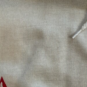 May include: Close-up of a beige knitted fabric with a blue and white stripe at the top. The fabric has a subtle texture and a slight sheen.