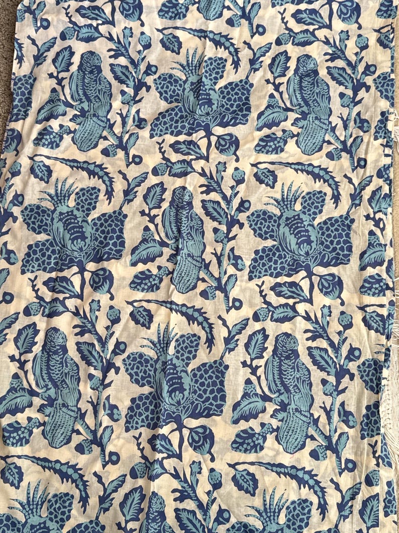 May include: A fabric with a repeating pattern of blue birds and floral designs on a cream background. The birds are perched on branches with leaves and flowers. The fabric has a vintage or bohemian aesthetic.