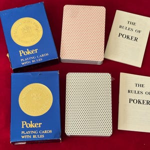 May include: Two blue poker card boxes with gold seals and the word "Poker" printed on them. Two decks of cards and two booklets titled "The Rules of Poker" are also visible. The card backs have a repeating pattern.