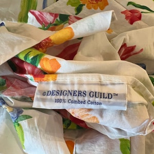 May include: White fabric with a floral print of tulips, leaves, and flowers in shades of red, orange, yellow, green, and blue. The fabric has a label that reads "&copy;DESIGNERS GUILD&trade; 100% Combed Cotton".