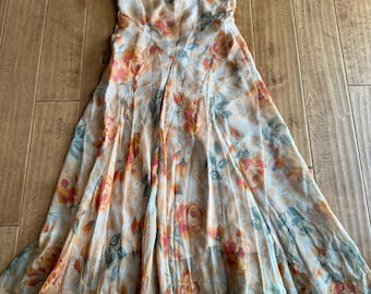 May include: A long, flowing floral dress with a light beige background and a pattern of orange and red roses. The dress has a ruffled neckline and short sleeves.