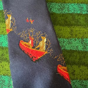 May include: Navy blue tie with a repeating embroidered design of foxes in a boat with red accents. The foxes are golden brown and the boat is red. The tie has a diagonal ribbed texture.