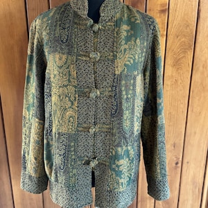May include: A green and gold patterned jacket with a mandarin collar and button closures. The jacket features an intricate paisley design and is displayed on a black mannequin head. The jacket's color palette includes shades of green, gold, and brown.