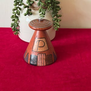 May include: A hand-painted ceramic salt and pepper shaker set in the shape of a teepee. The teepee is decorated with geometric patterns in shades of brown, blue, and black. The top of the teepee has a small, silver knob.