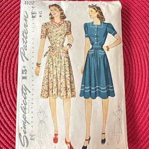 May include: Vintage Simplicity sewing pattern number 4102 for a dress. The pattern is for size 12 with a bust measurement of 30 inches. The pattern shows two versions of the dress, one with a floral print and the other in a solid blue color. Both dresses have a fitted bodice, a full skirt, and short sleeves.