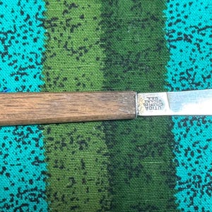 May include: A small knife with a straight wooden handle and a silver-colored metal blade. The blade features an etched stamp that reads Utica Cutlery Co. U.S.A. The handle has a pointed end, and the blade has a curved, pointed tip.