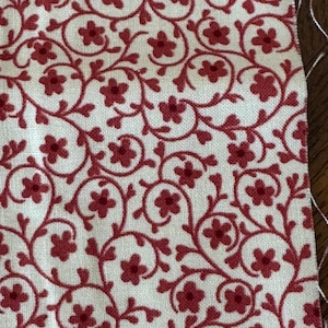 Puede incluir: Patrón floral rojo sobre un fondo de tela blanco. El patrón presenta pequeñas flores rojas y enredaderas en espiral.