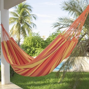 May include: A fabric hammock featuring a vibrant striped pattern in shades of orange, yellow, and red. The hammock is suspended by thick, matching orange cords attached to a white pillar, showcasing a woven design with a deep, curved centre.