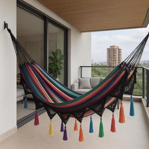 May include: A colorful hammock with rainbow stripes hangs on a balcony. The hammock has black fringe and tassels in various colors, including blue, orange, yellow, and purple. The background includes a city view.