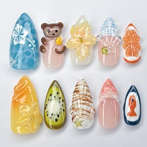 May include: A collection of ten nail art designs. The designs include a blue nail with a white floral design, a brown bear, a yellow flower, a pink nail with a blue and white pattern, an orange slice, a yellow flower, a kiwi slice, a seashell, a pink nail with a red top, and a blue boat with a fish.