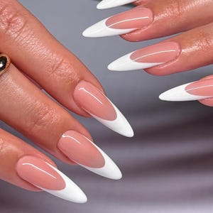 May include: Close-up of long, almond-shaped nails with a classic French manicure. The nails feature a pale pink base with a crisp white tip. The manicure is glossy and well-manicured, showcasing a timeless nail design.