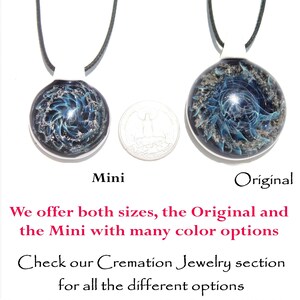 May include: Two glass cremation jewelry pendants, one labeled "Mini" and the other "Original." Both are round with a swirling blue with ashes design. The pendants hang from black cords with white clasps. A quarter is placed between the pendants for size comparison.