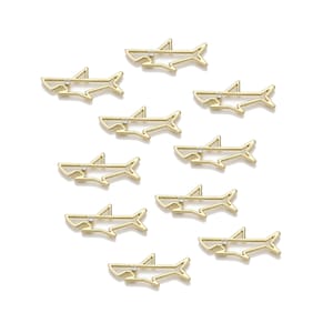May include: Gold-colored shark charms with a small, clear gem embedded in the mouth area. The charms are arranged on a white background. The shark charms are a fun, nautical-themed accessory.