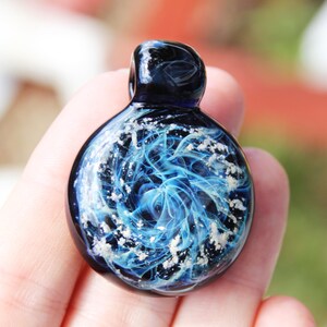 Close-up of black glass pendant containing pet ashes on a black adjustable cord. Featured on woman's hand for size comparison. Made to order by DragonFire Glass