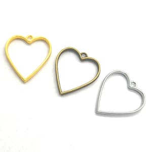 May include: Three heart-shaped metal charms in gold, bronze, and silver. Each charm has a loop at the top for attaching to jewelry or other crafts. The charms are empty in the center, creating a frame.