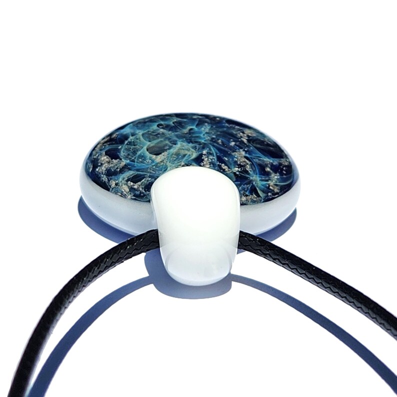 A handcrafted urn pendant necklace featuring a round, blue with mixed in ashes glass pendant with a white bail. The pendant is suspended from a black cord. The glass pendant has a unique, swirling design.